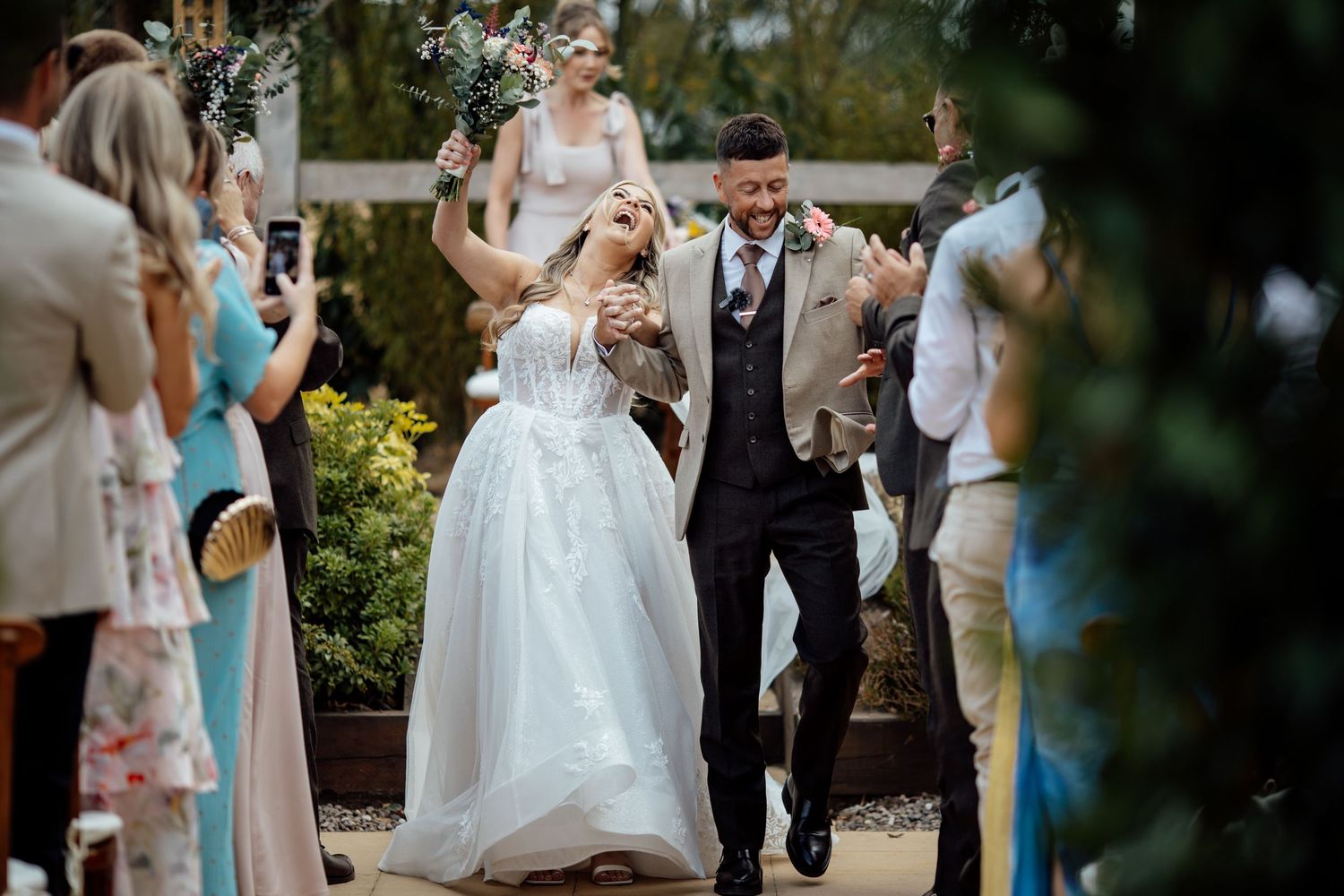 Joyful newlyweds walk down the aisle at an outdoor garden wedding ceremony.