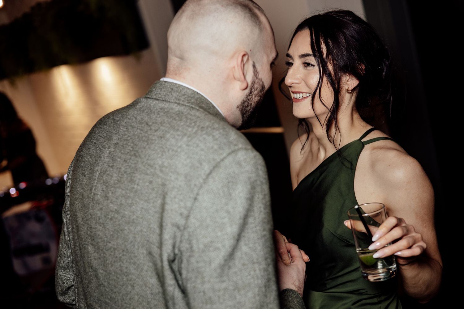 Woman in green dress smiling and holding a drink while talking with a man.