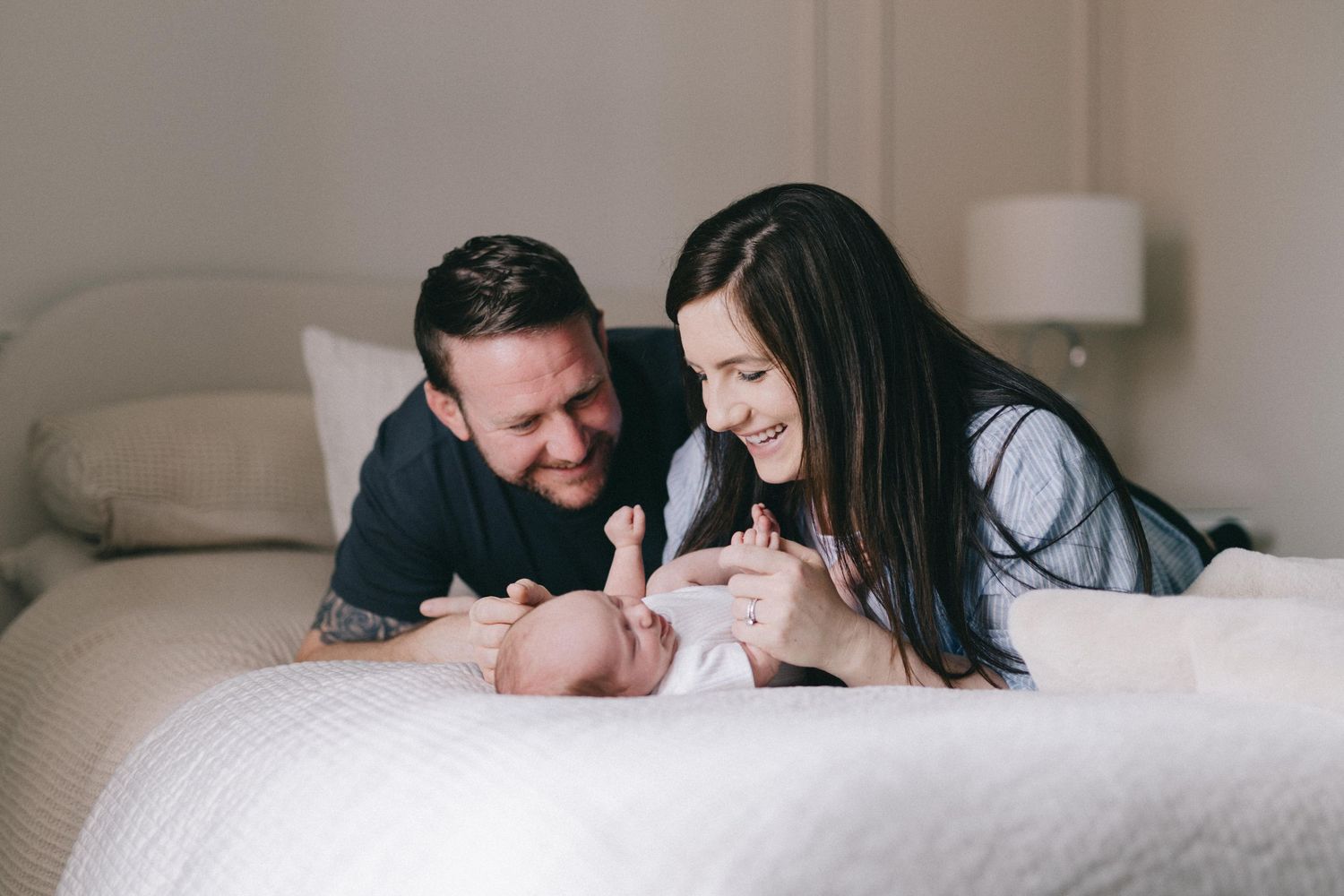 Happy parents lying on bed smiling at their newborn baby during an intimate family lifestyle photography session.