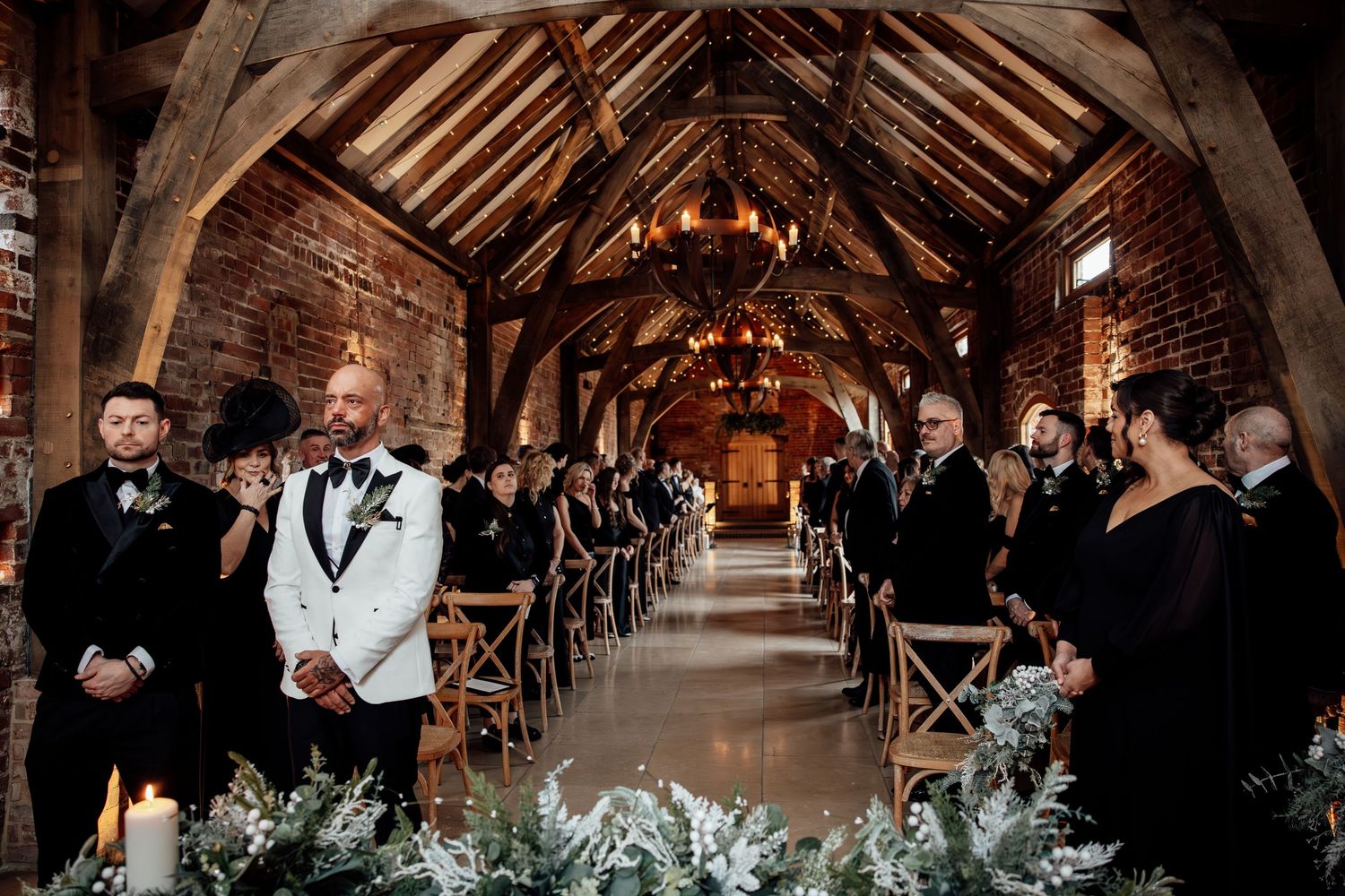 Rustic barn wedding ceremony setup with wooden beams and romantic chandelier lighting.