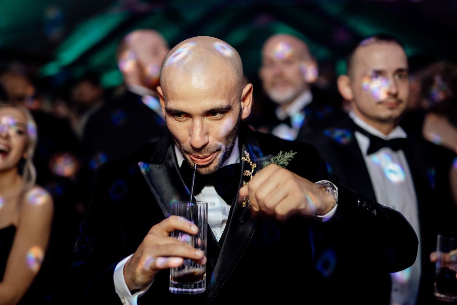 Wedding guests in formal attire celebrate during an evening reception with dramatic lighting.