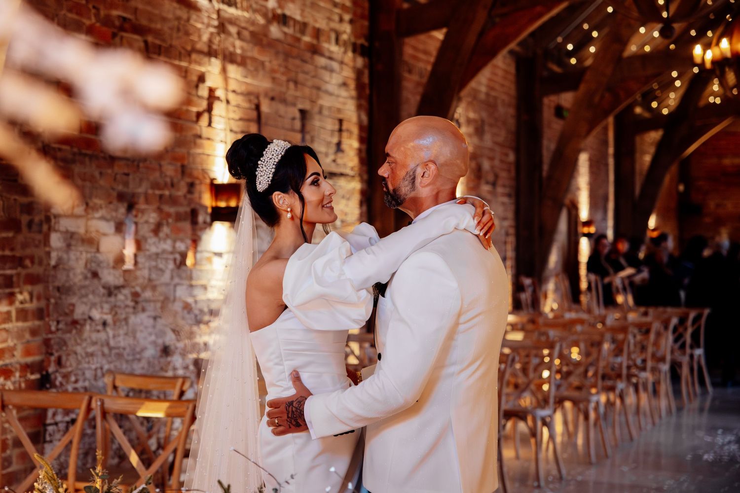 Couple shares an intimate dance moment in front of exposed brick walls with twinkling lights at wedding reception.