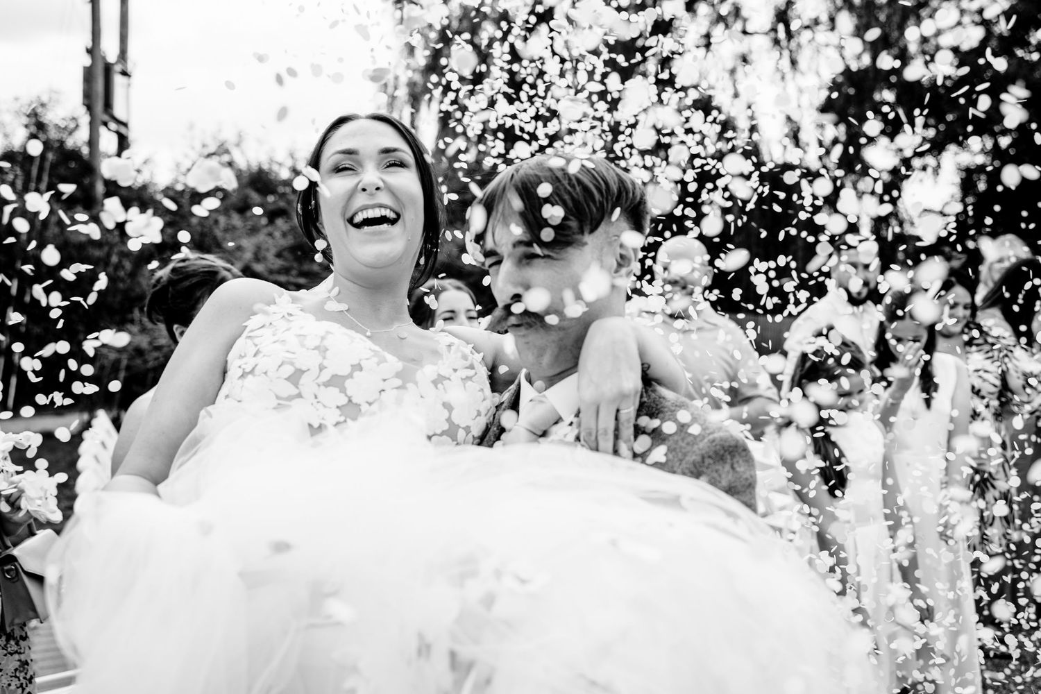 Black and white portrait of someone in wedding dress with small dog outdoors.