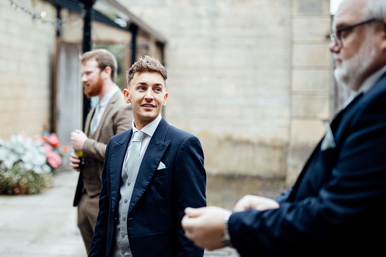 Wedding guests chat and interact outside a stone building.