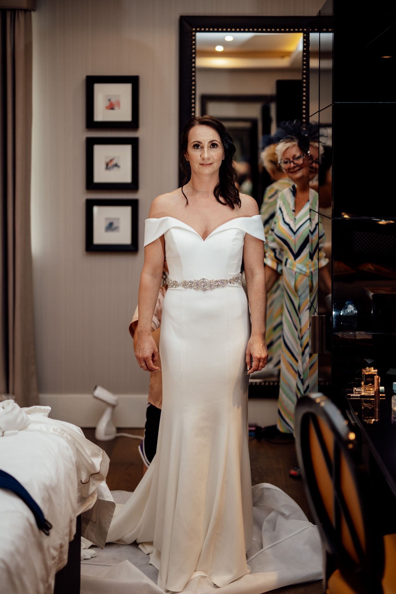 Elegant white wedding dress displayed in a room with framed artwork on walls.