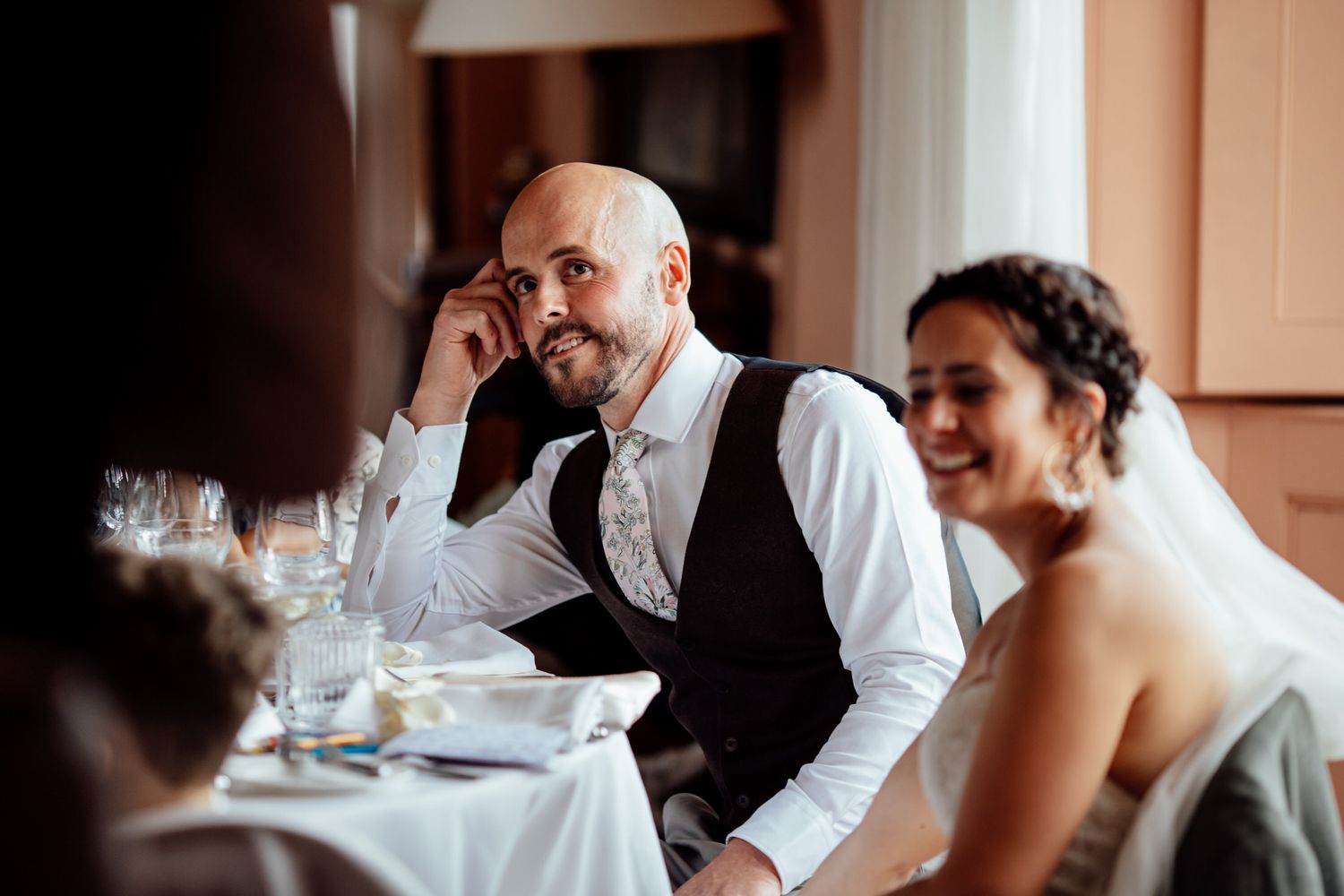 Wedding guests enjoy an intimate indoor reception at elegant tables with glassware.