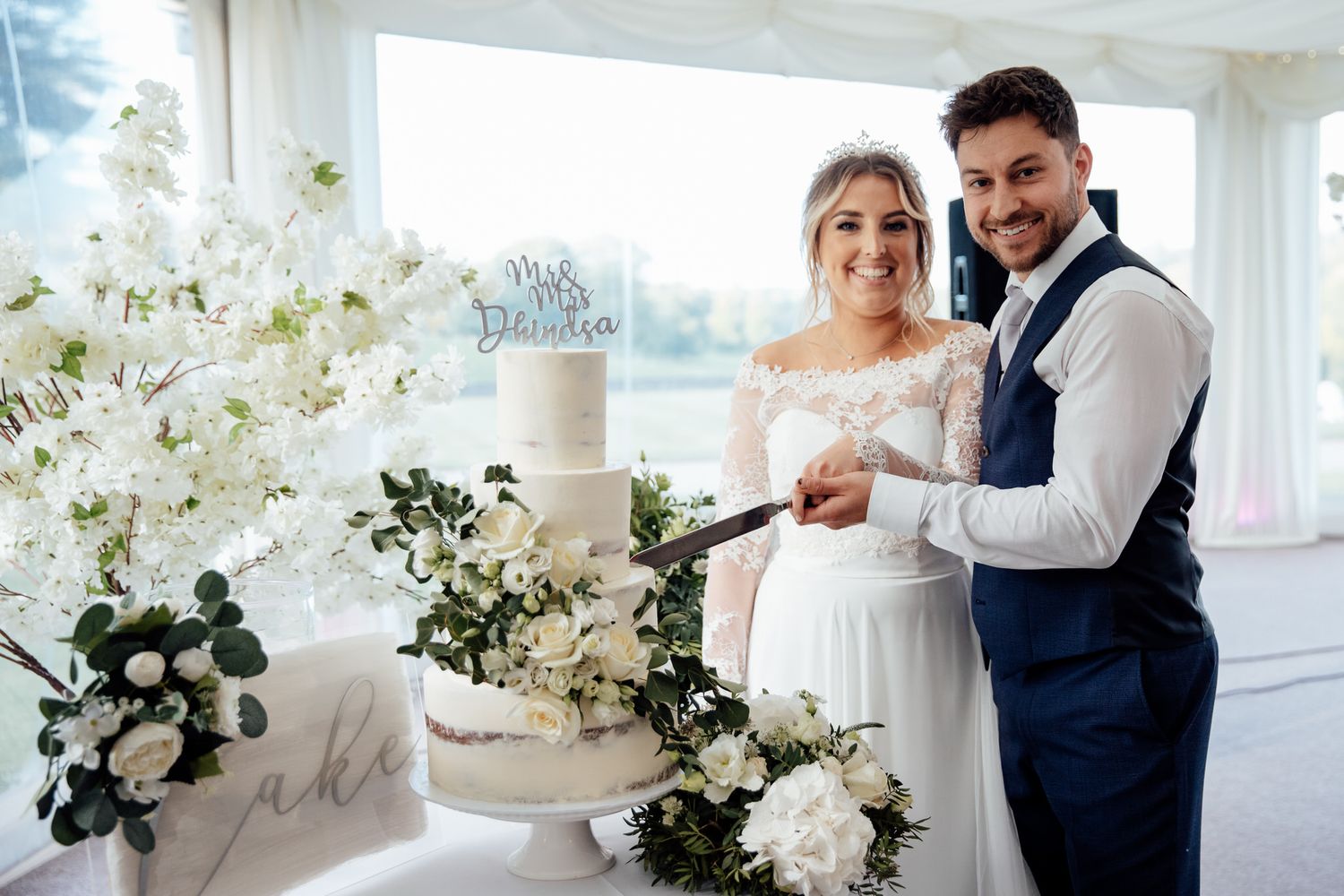 Elegant white wedding cake display with floral decorations in a bright indoor setting.