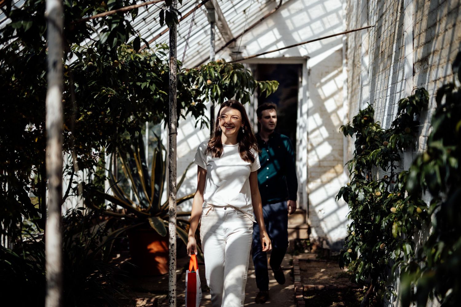 Couple sharing romantic moments in a sunlit greenhouse setting.