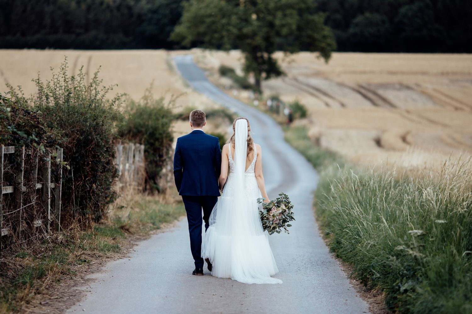 A couple walks along a countryside path surrounded by wheat fields.