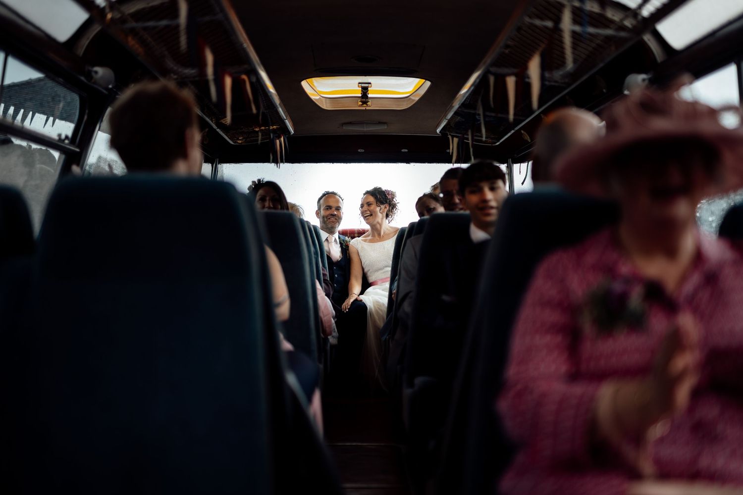View down the aisle of a wedding party bus with passengers seated inside.