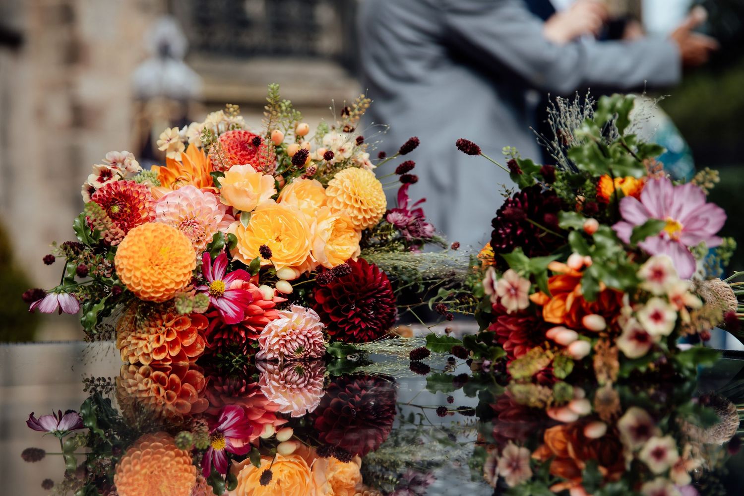 Stunning floral arrangement with orange and burgundy blooms reflects in glossy surface.