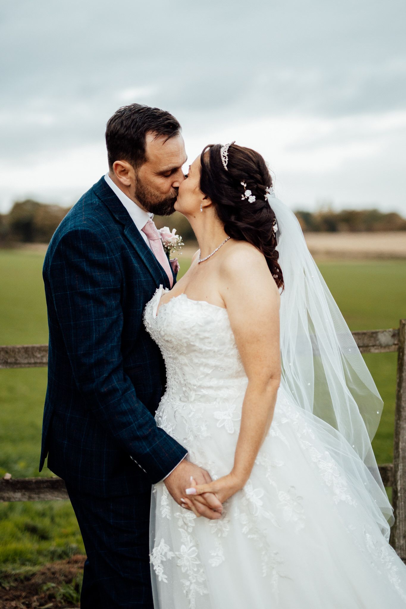 Romantic countryside wedding portraits with stone wall and open field backdrop.