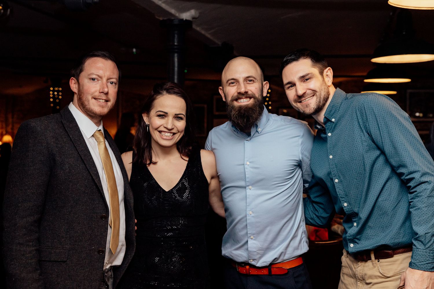 Wedding guests gather and socialize at an indoor reception with warm lighting.