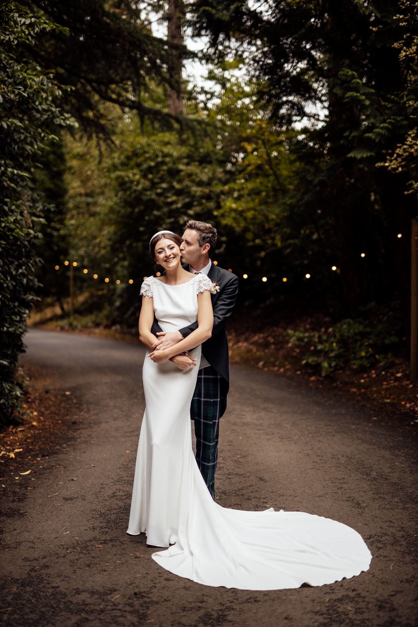 Newlyweds share an intimate moment on a wooded path with the bride's dress trailing behind.