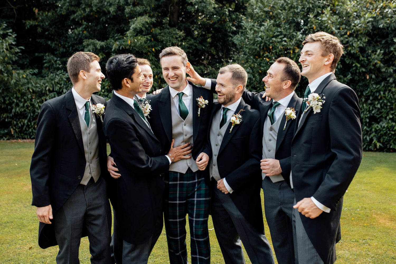 Groomsmen in black suits sharing laughs during outdoor wedding photos.