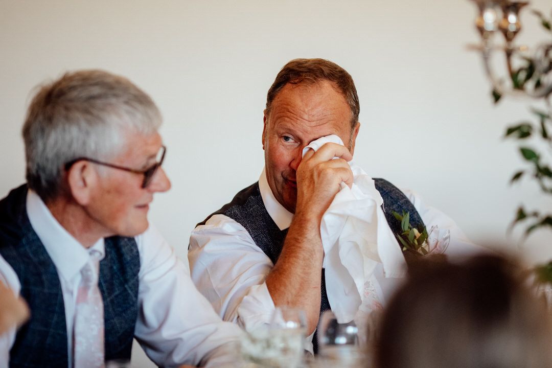 Emotional reactions during wedding speeches in rustic indoor venue.