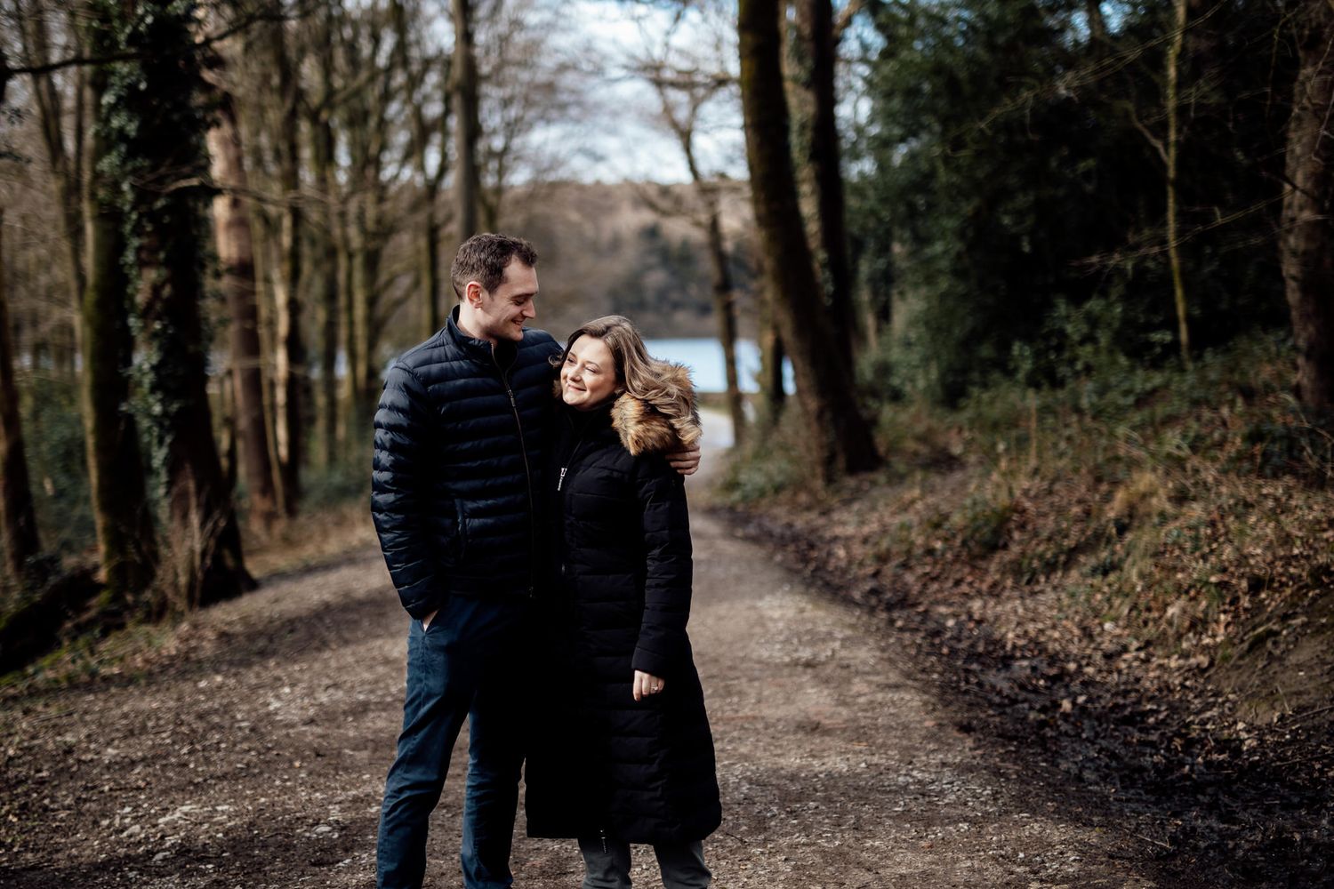 A couple takes a romantic walk through a wooded trail on a winter afternoon.