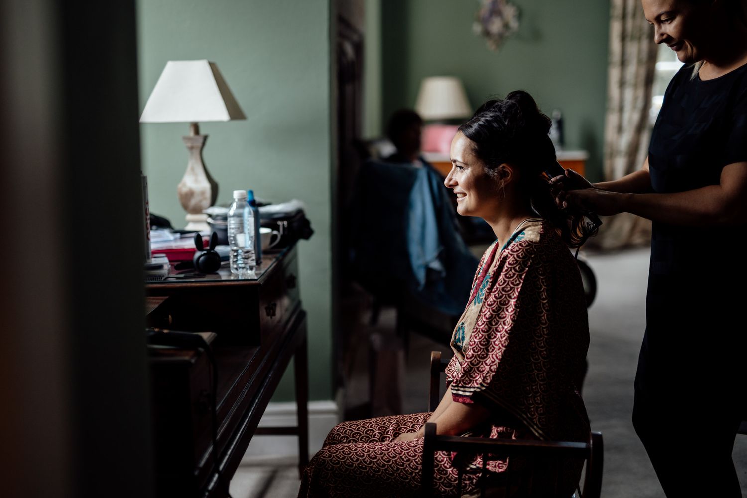 Wedding preparation scene in a dimly lit room with soft window light.