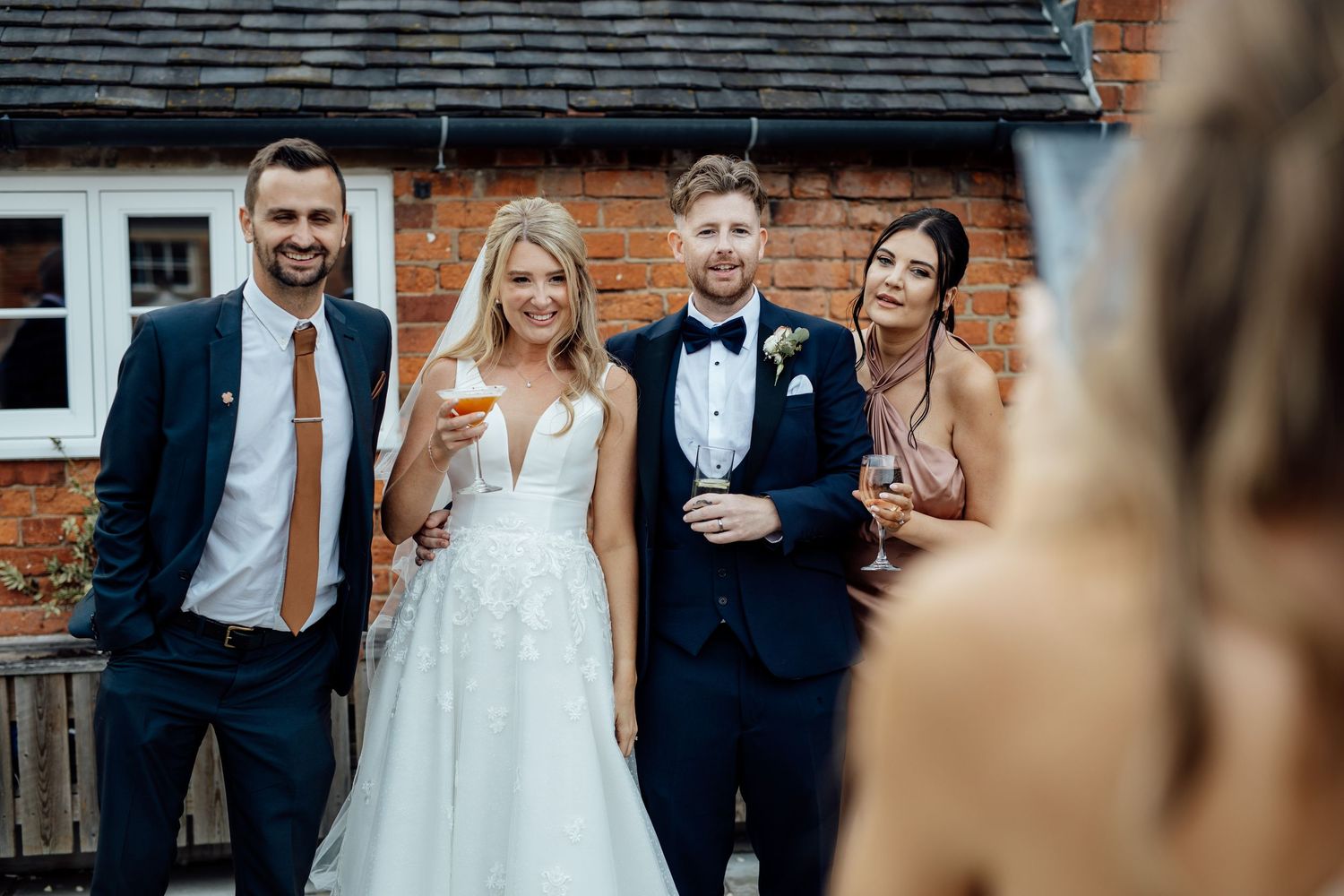 Wedding party celebrates outside brick venue with joyful expressions.