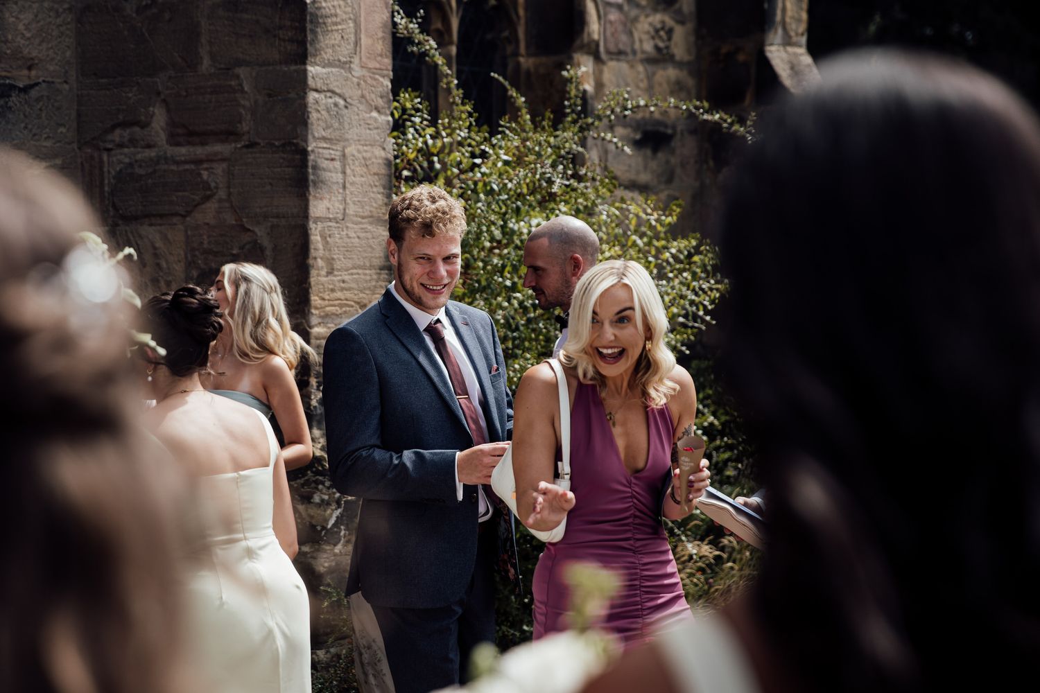 Wedding ceremony guests gather outside a stone church building.