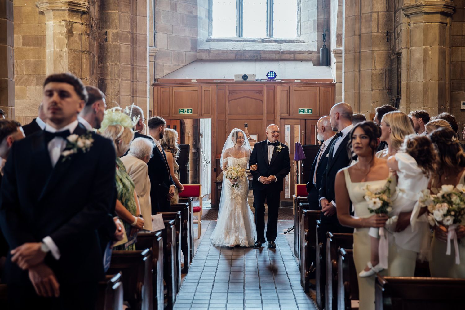 Wedding ceremony in progress inside historic church with stone columns and stained glass windows.