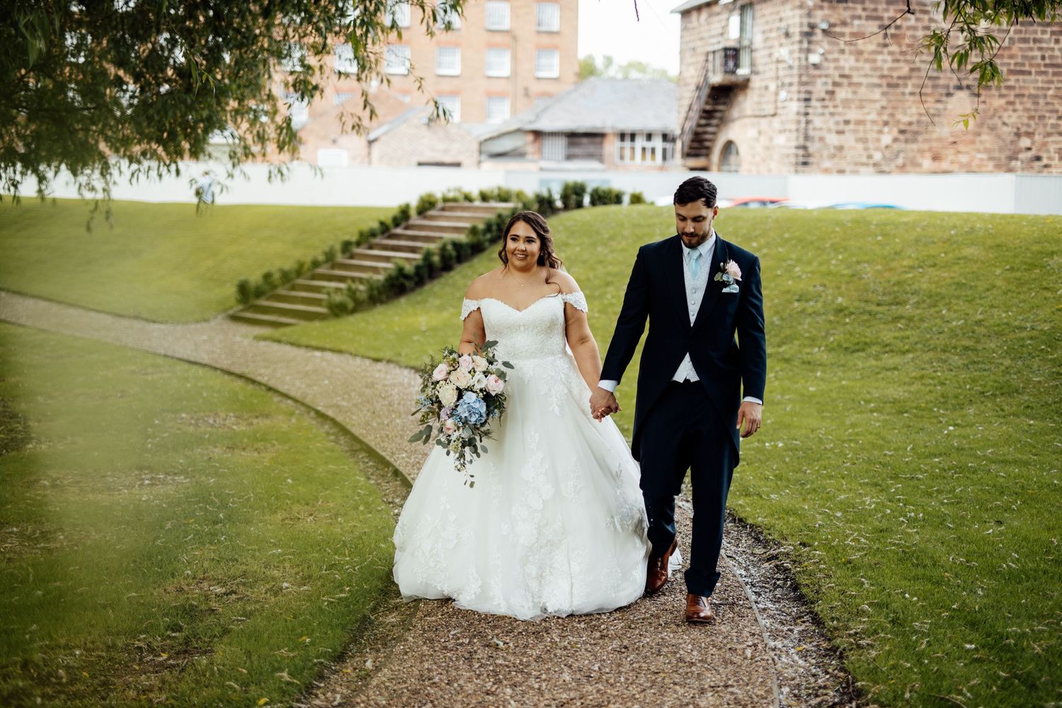 Couple walking along garden path at historic venue on wedding day.