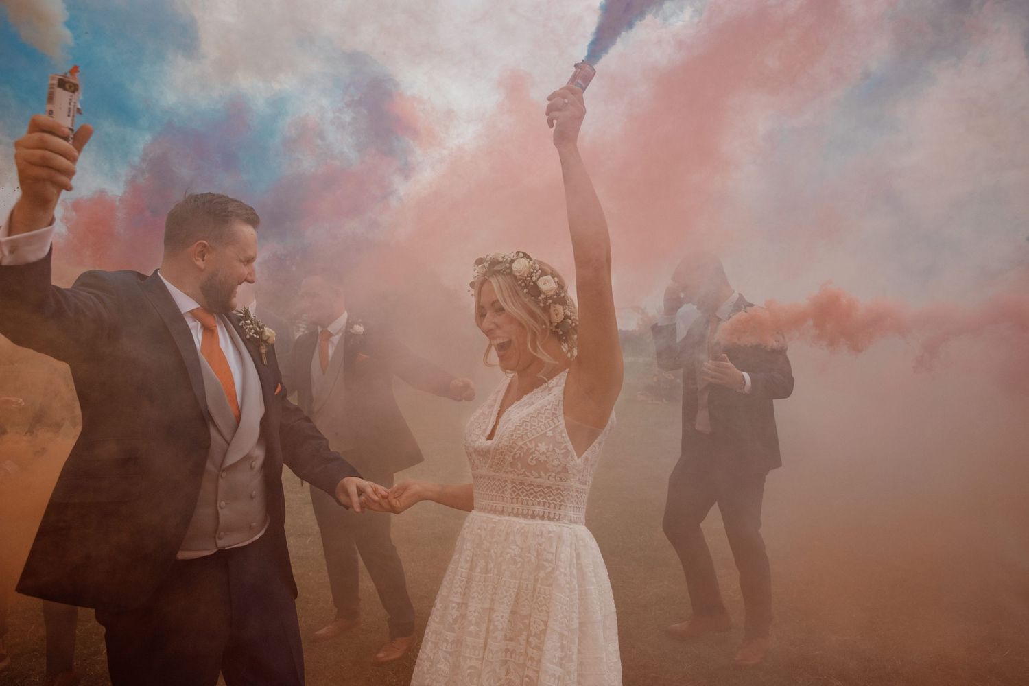A wedding celebration with pink smoke bombs creating a dreamy atmosphere outdoors.