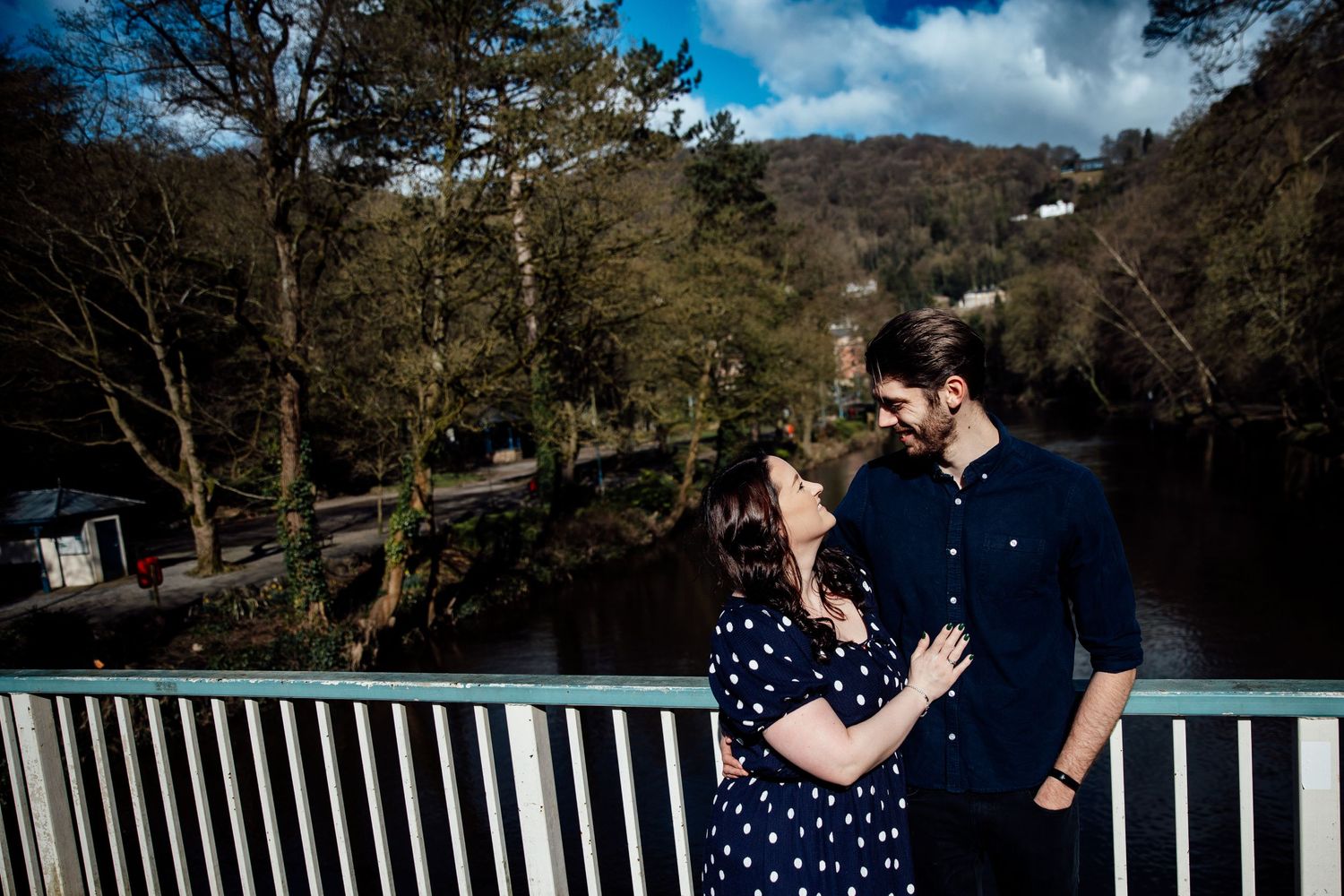 A couple shares an intimate moment on a bridge overlooking a scenic river valley.