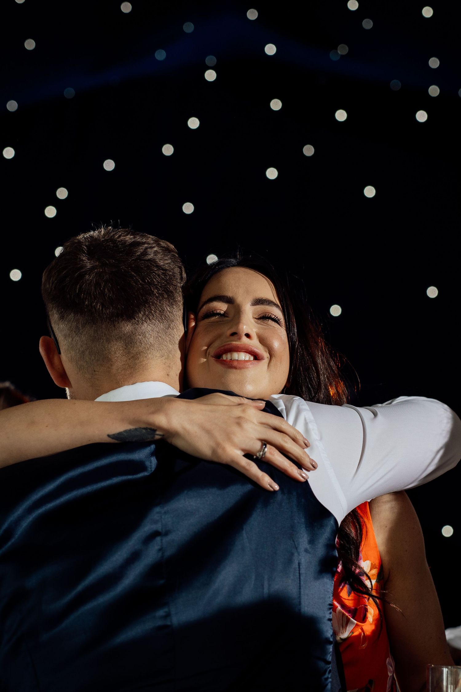 Couple embracing in front of twinkling lights creating a romantic atmosphere.