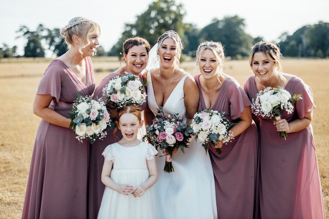 Joyful bridal party with flower girl sharing genuine laughter while holding bouquets.