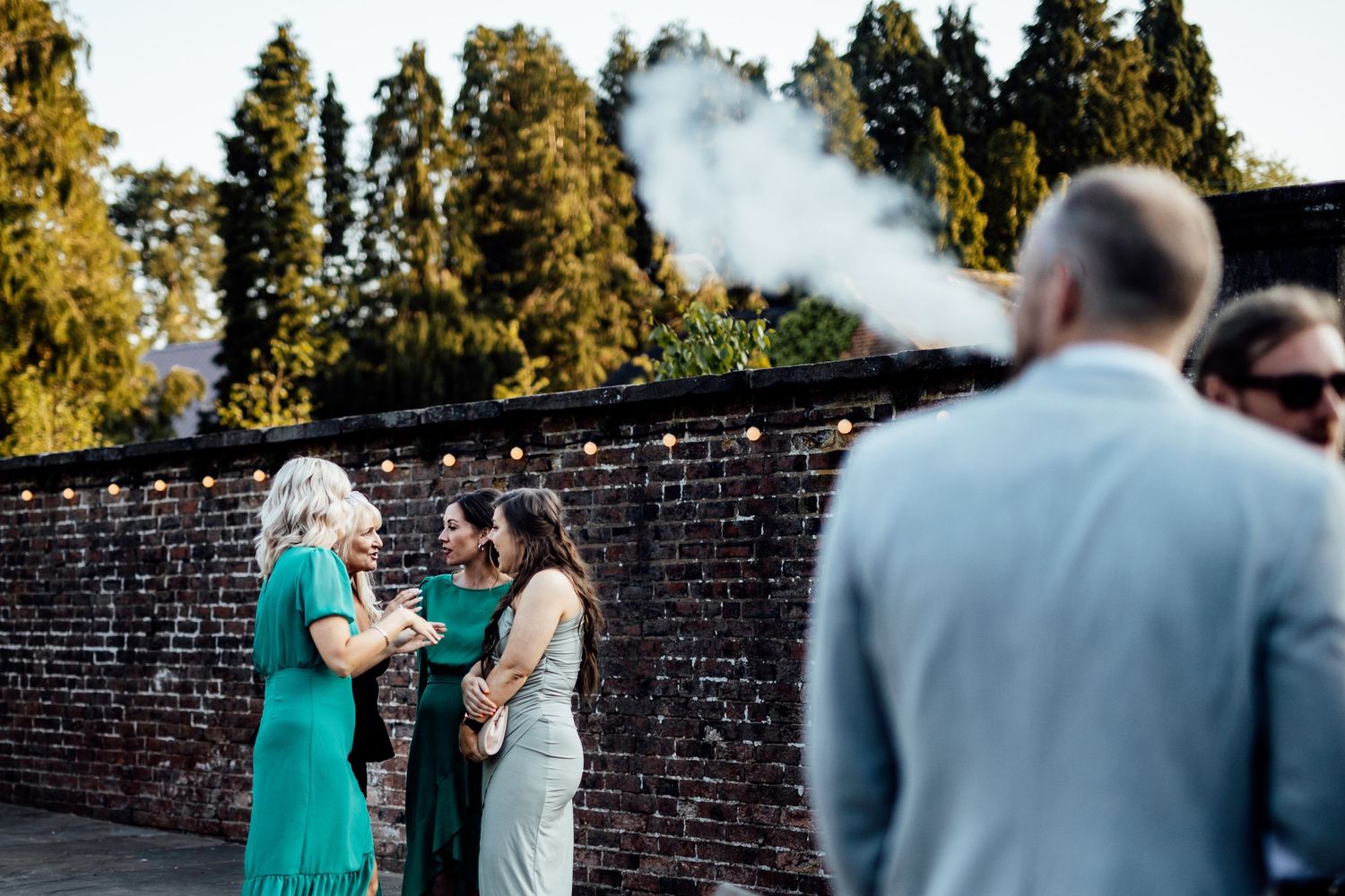 Smoke creates a dramatic effect against sunlit trees during an outdoor wedding ceremony.