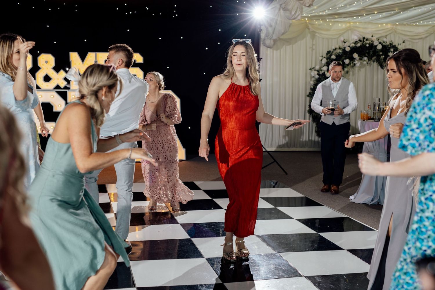 Wedding guests dance and celebrate on a black and white checkered dance floor.