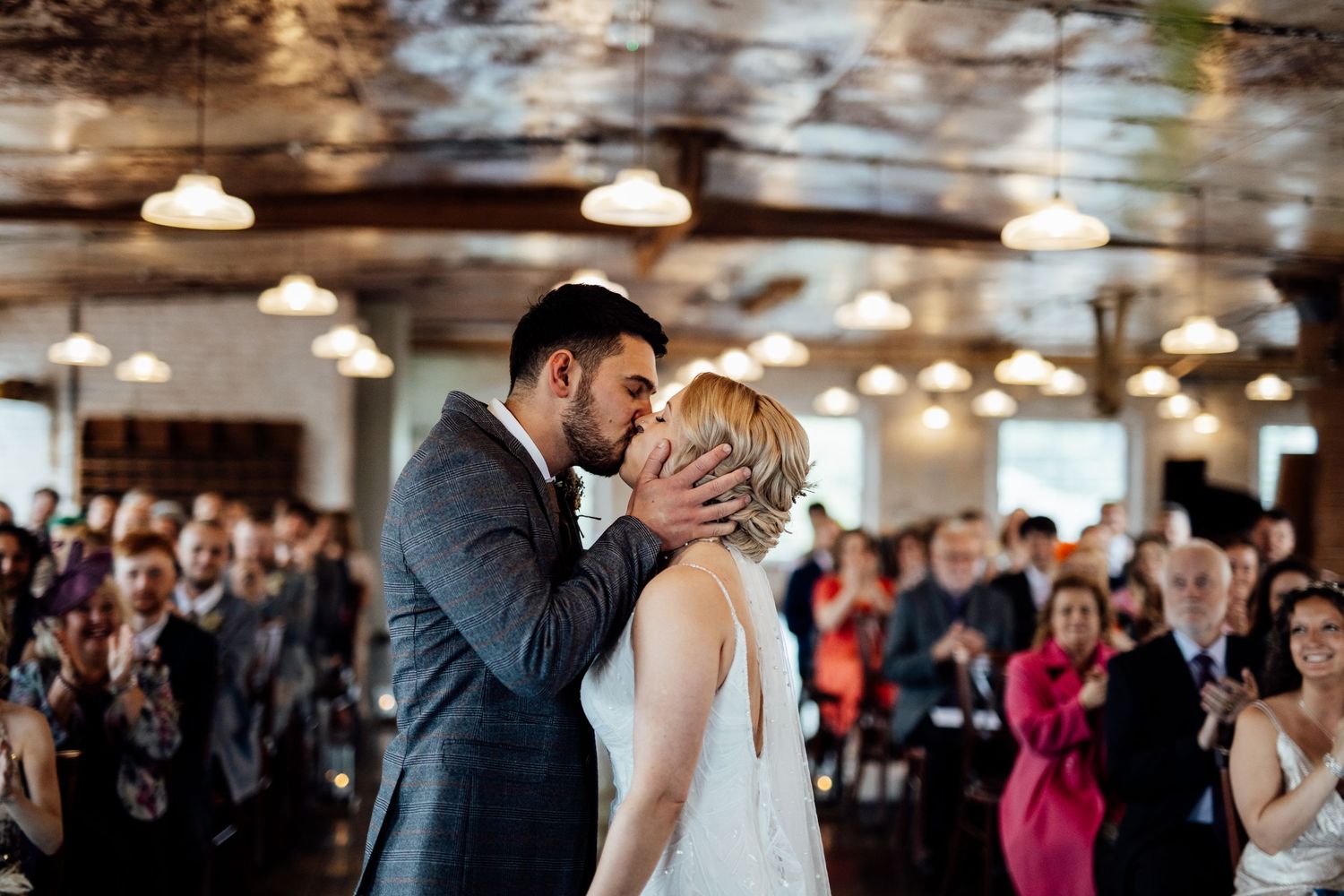 Wedding ceremony celebration in an indoor venue with industrial lighting and exposed brick walls.