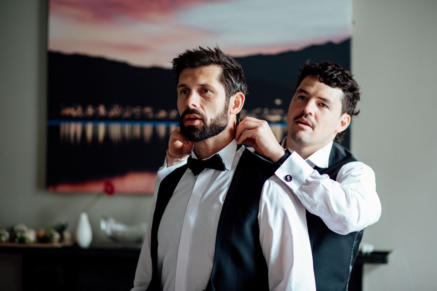 Groomsmen helping each other prepare and adjust formal attire.