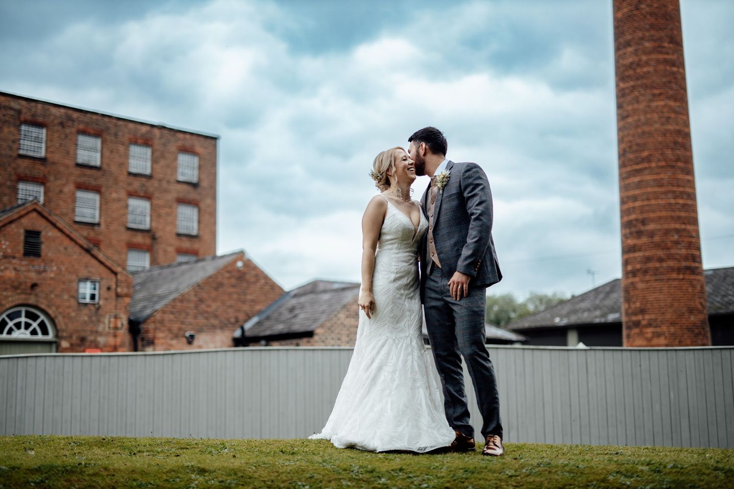Historic brick industrial building provides backdrop for wedding photos on cloudy day.