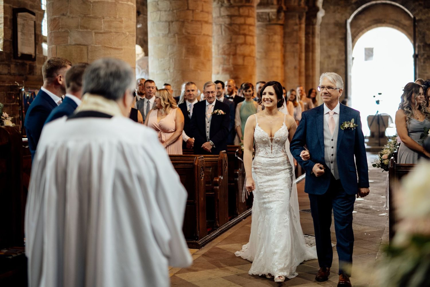 Wedding ceremony procession in historic stone church with arched columns.