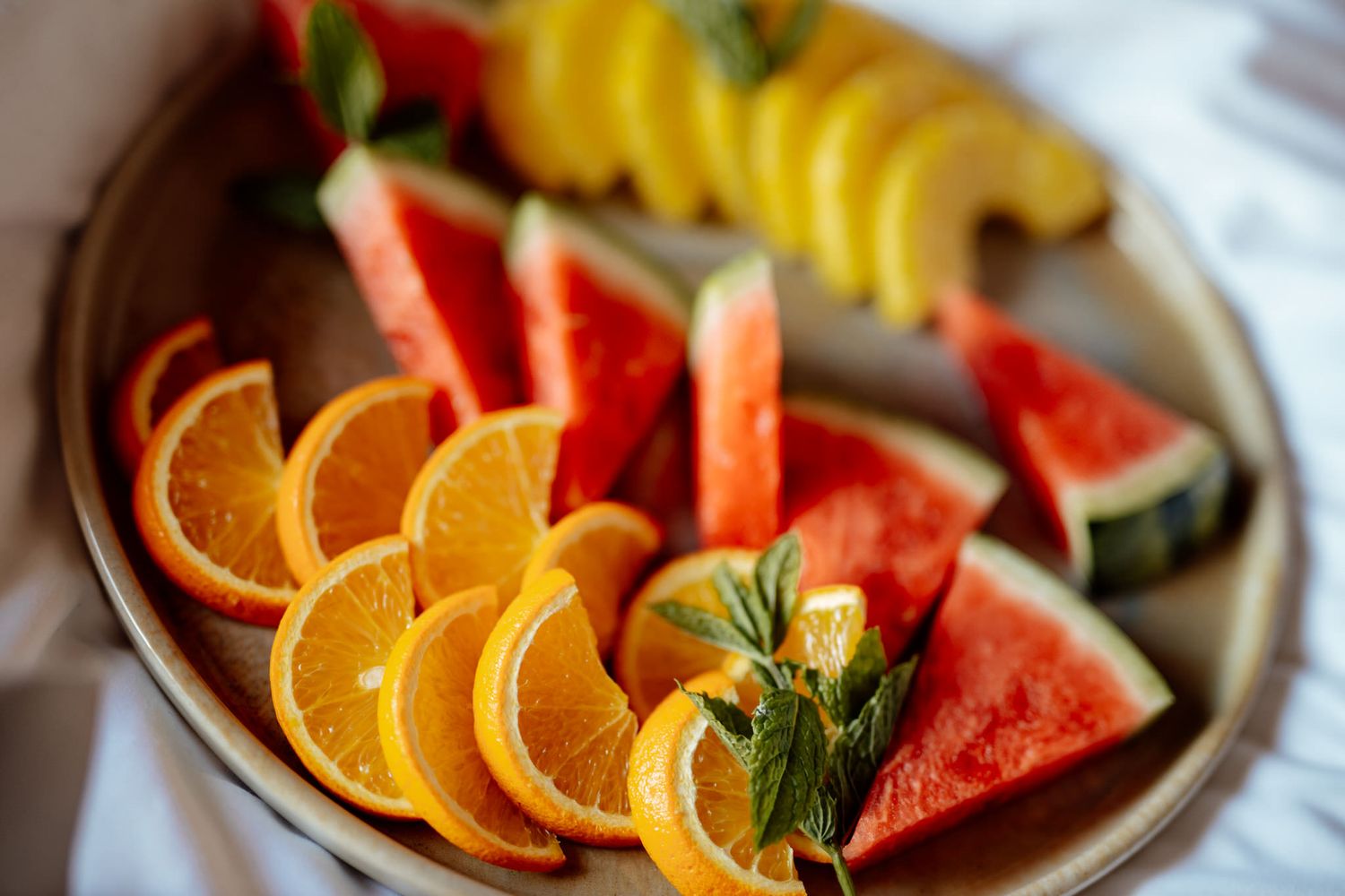 Fresh fruit platter with sliced oranges and watermelon arranged on a wooden serving board.