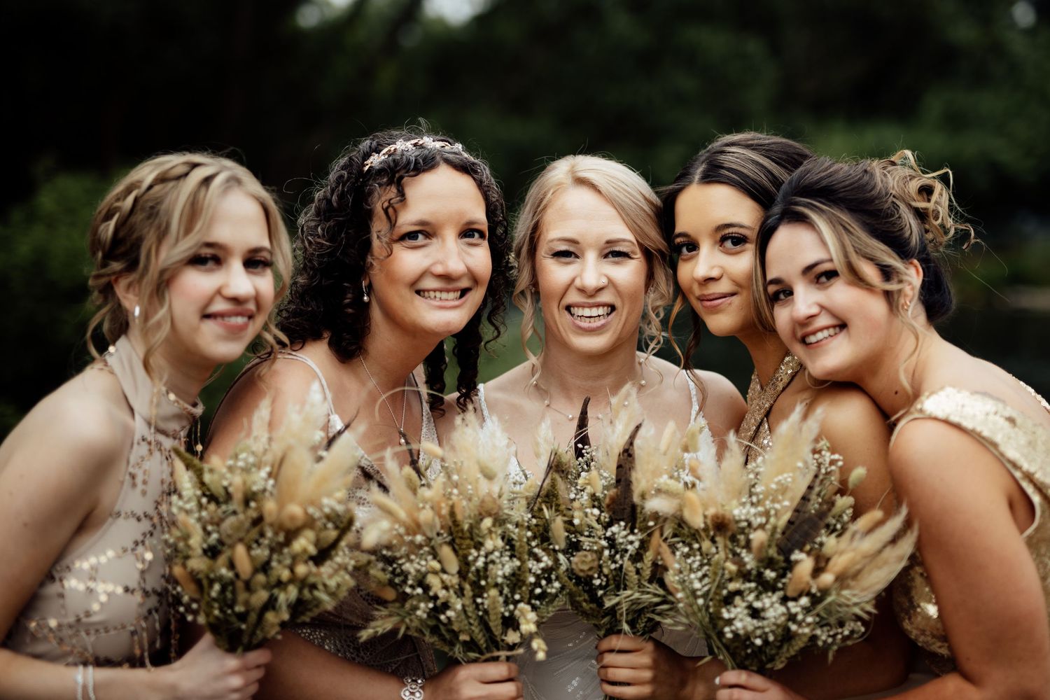 Bridesmaids in sparkly dresses hold bouquets while posing outdoors.