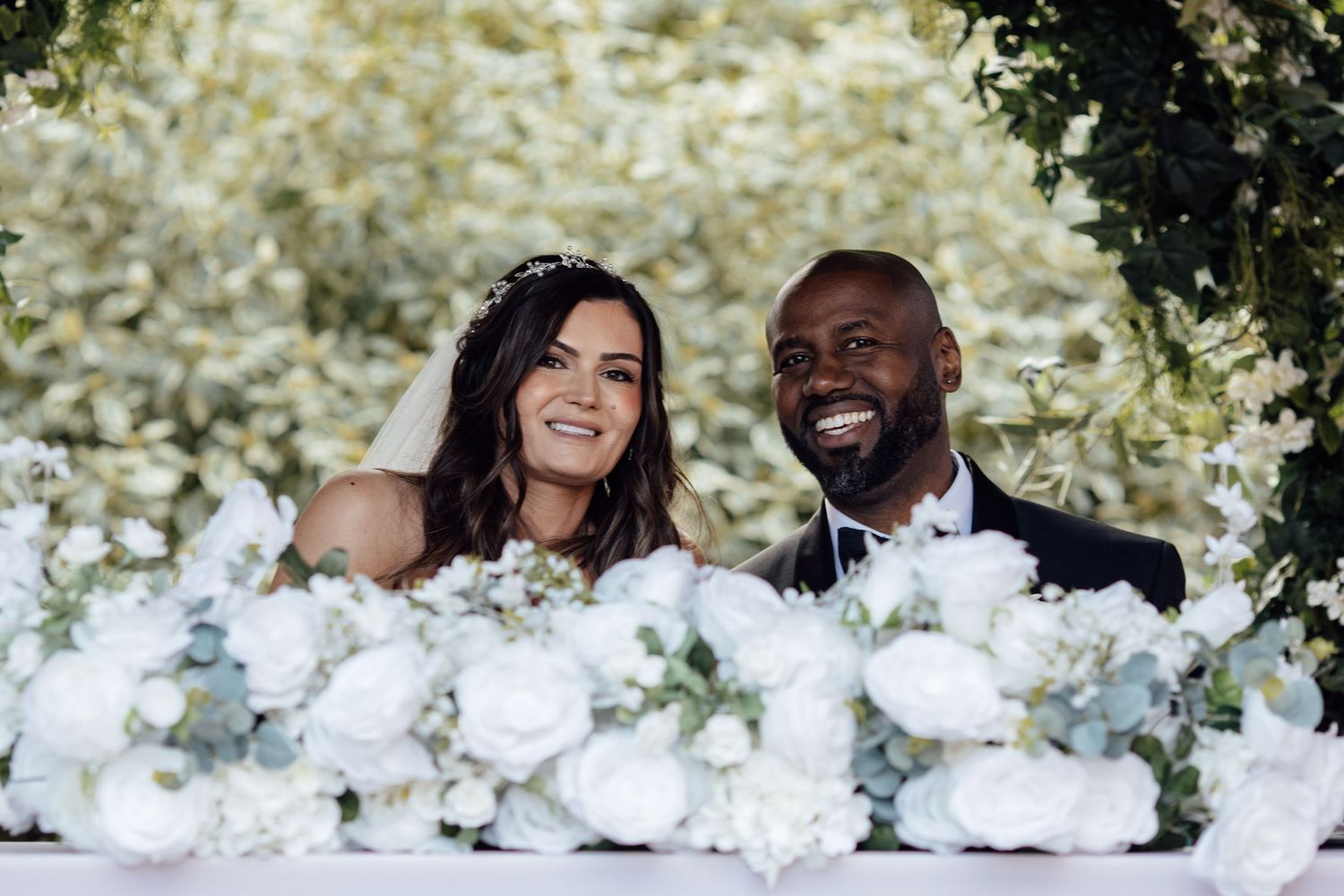 Wedding couple poses behind romantic white floral arrangements at their reception.