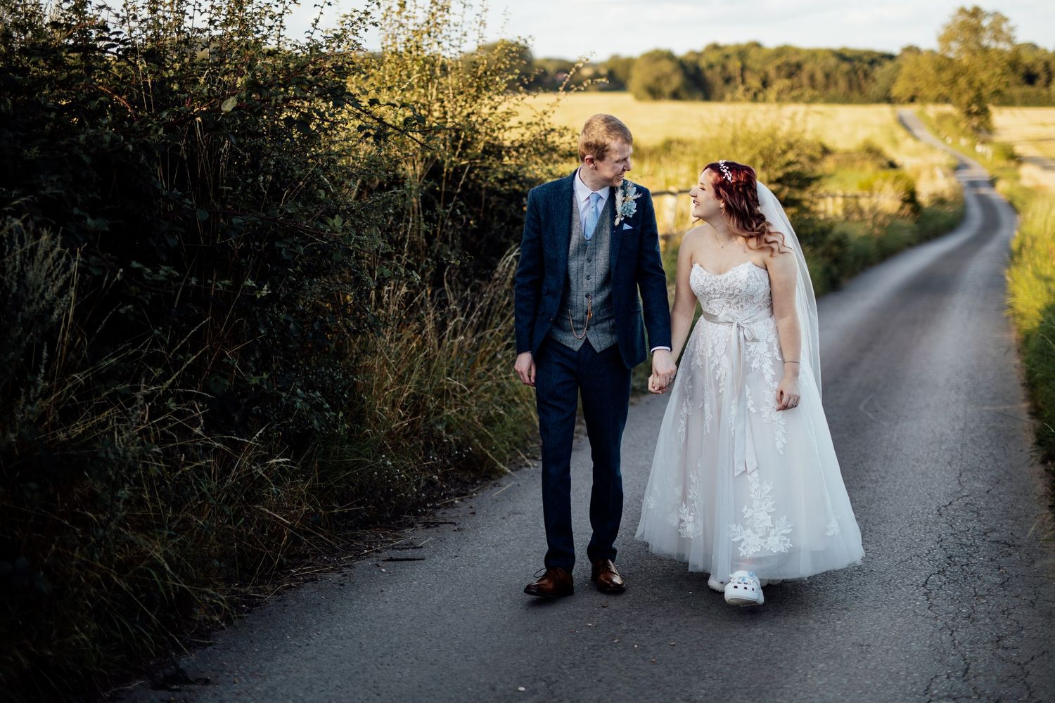 Wedding couple walking along a countryside path during sunset photography session.