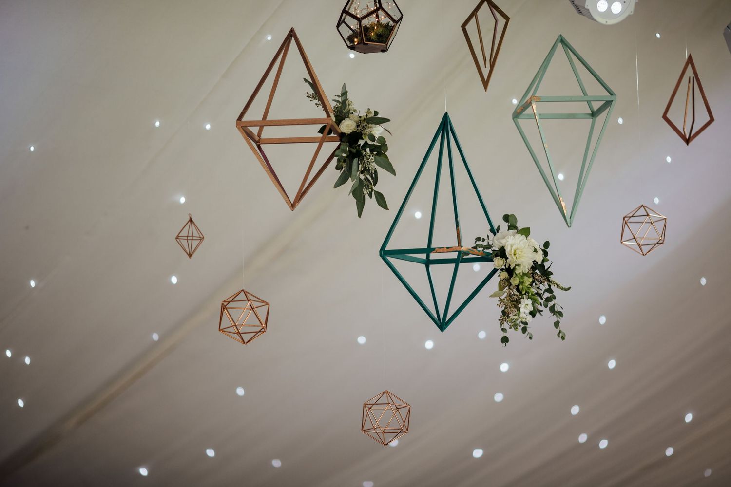 Modern geometric hanging decorations with greenery and twinkle lights on a white ceiling.