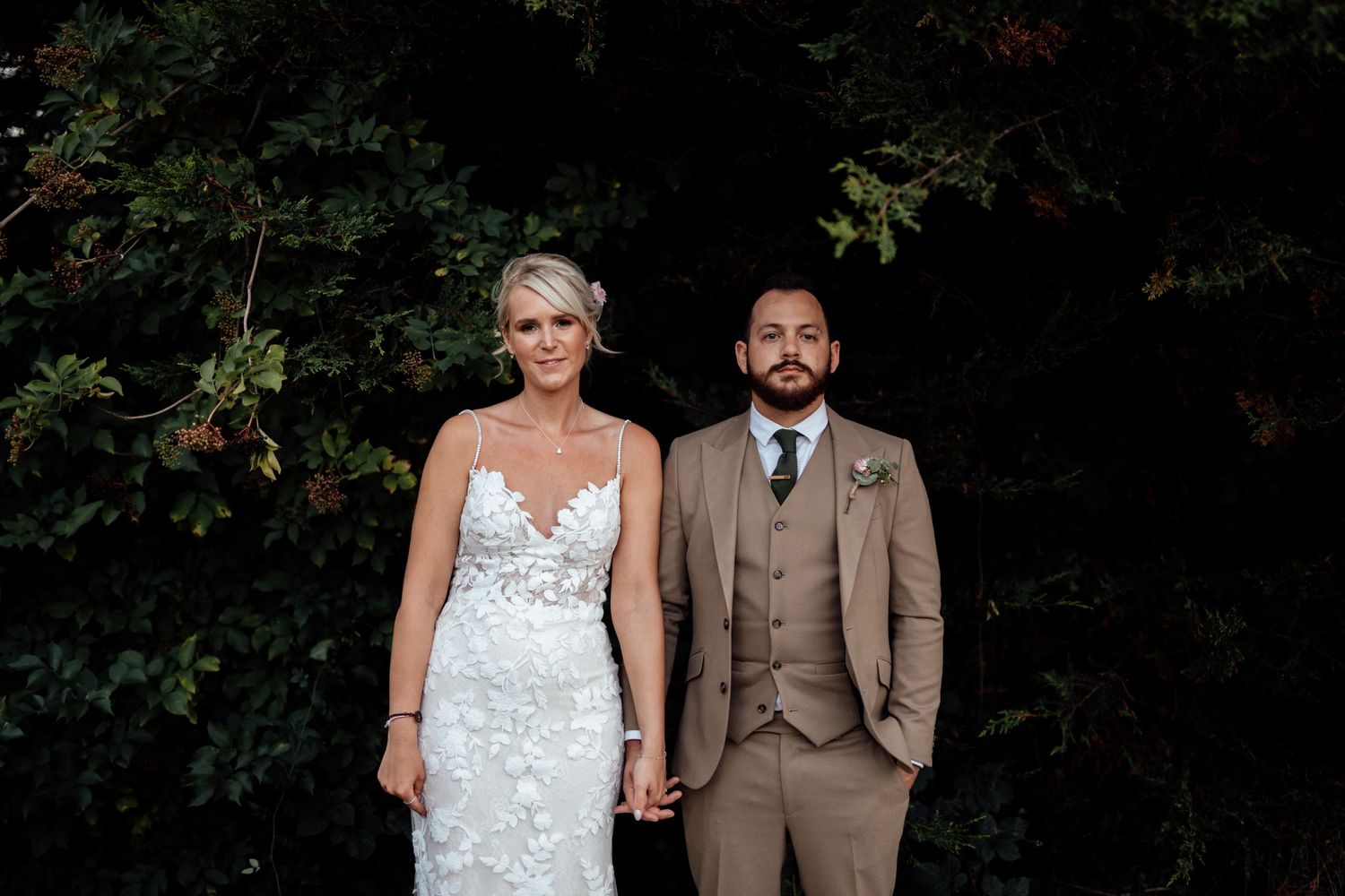 Couple poses for romantic outdoor wedding portraits against natural greenery.