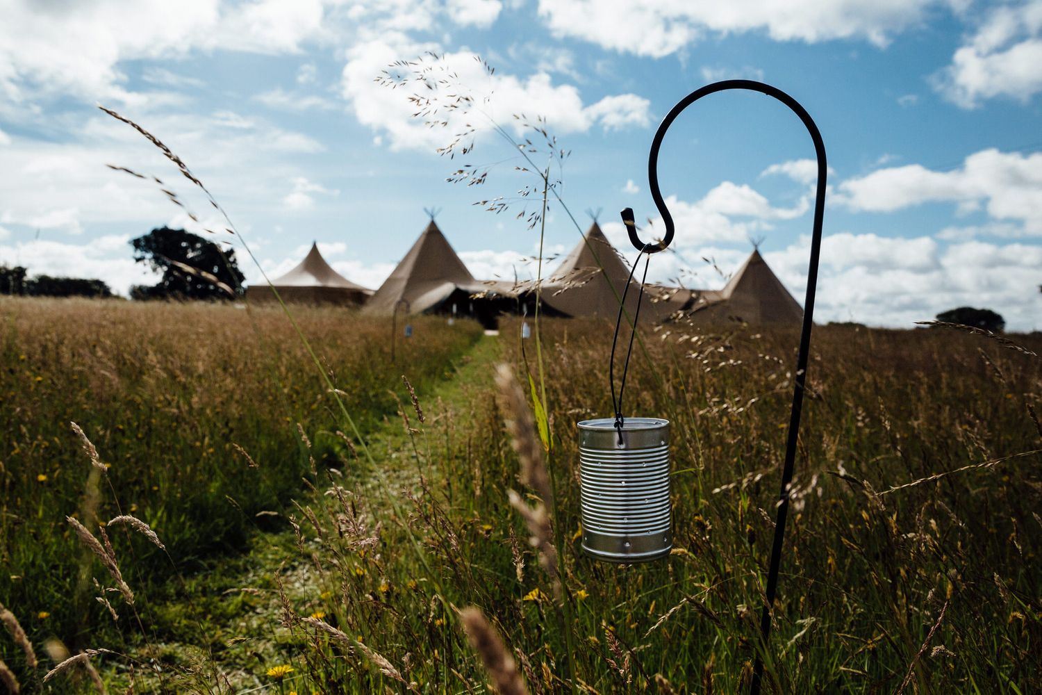 Pastoral field landscape with teepee tents and decorative lanterns under cloudy blue skies.