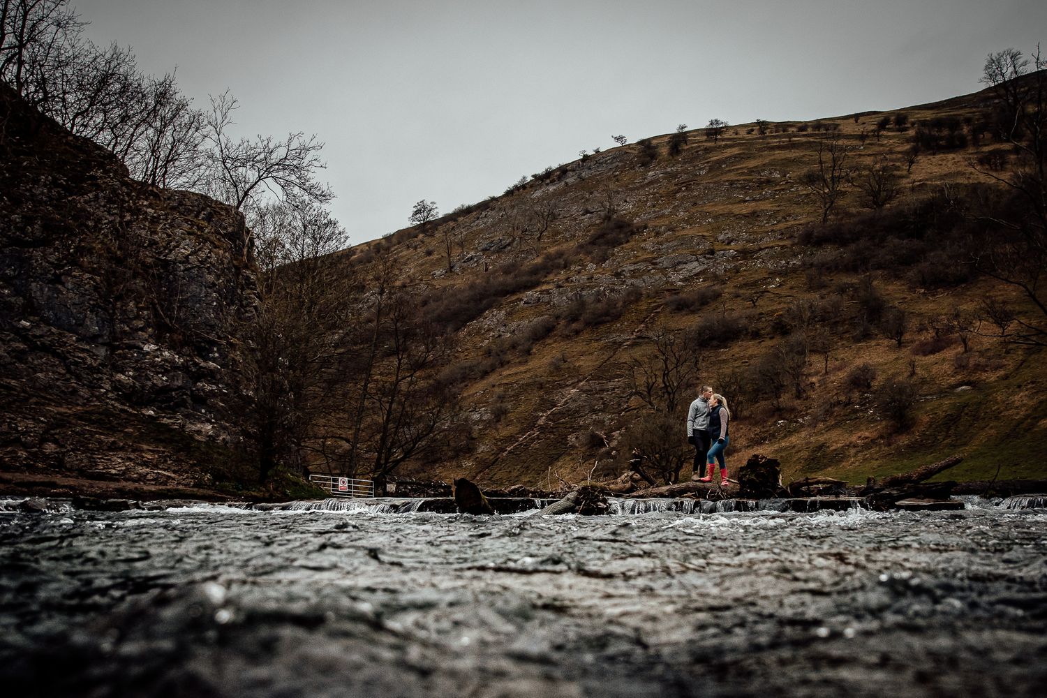 A dramatic landscape of rocky hills and flowing water in muted tones.