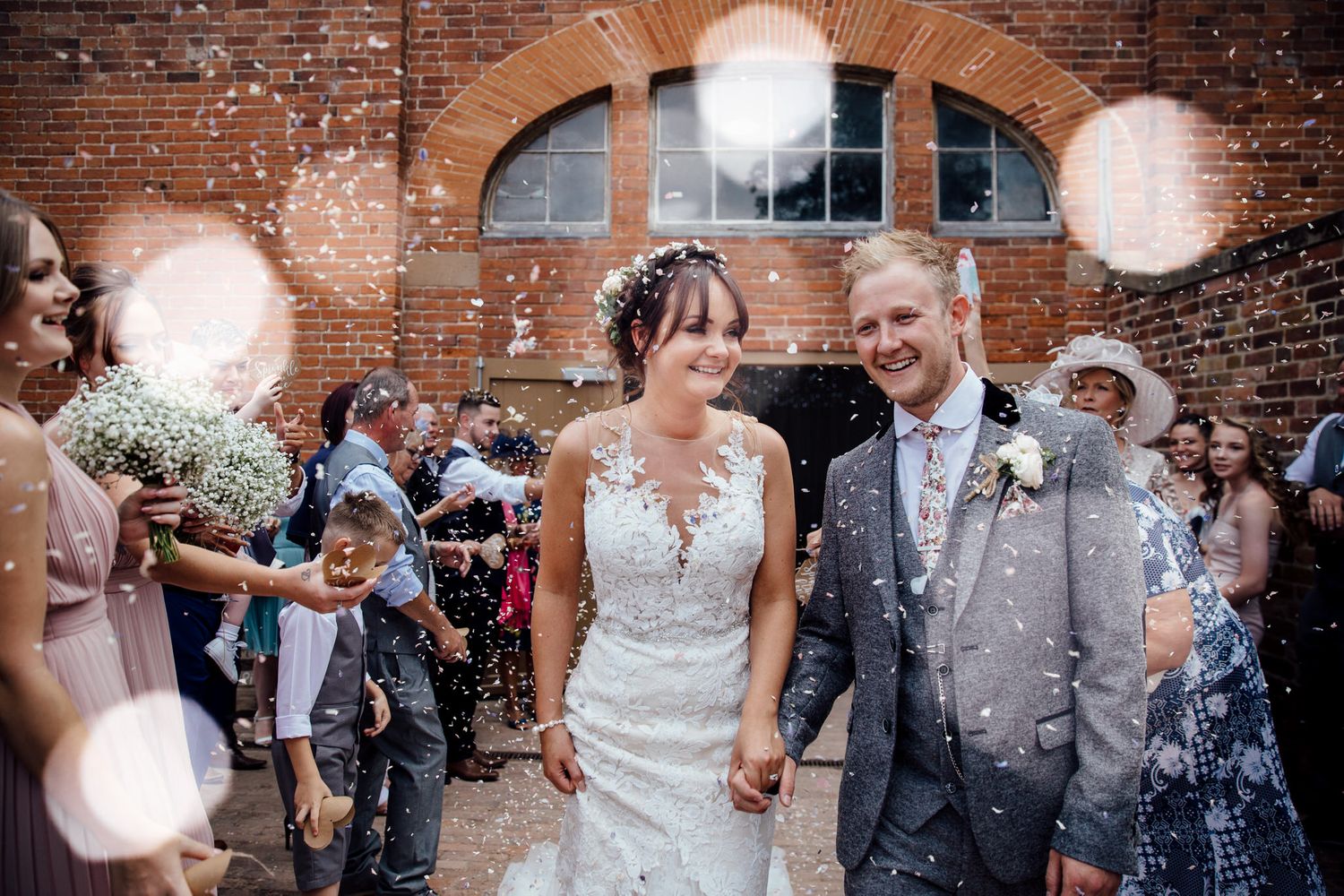 Confetti shower celebration outside a rustic brick venue with arched windows.