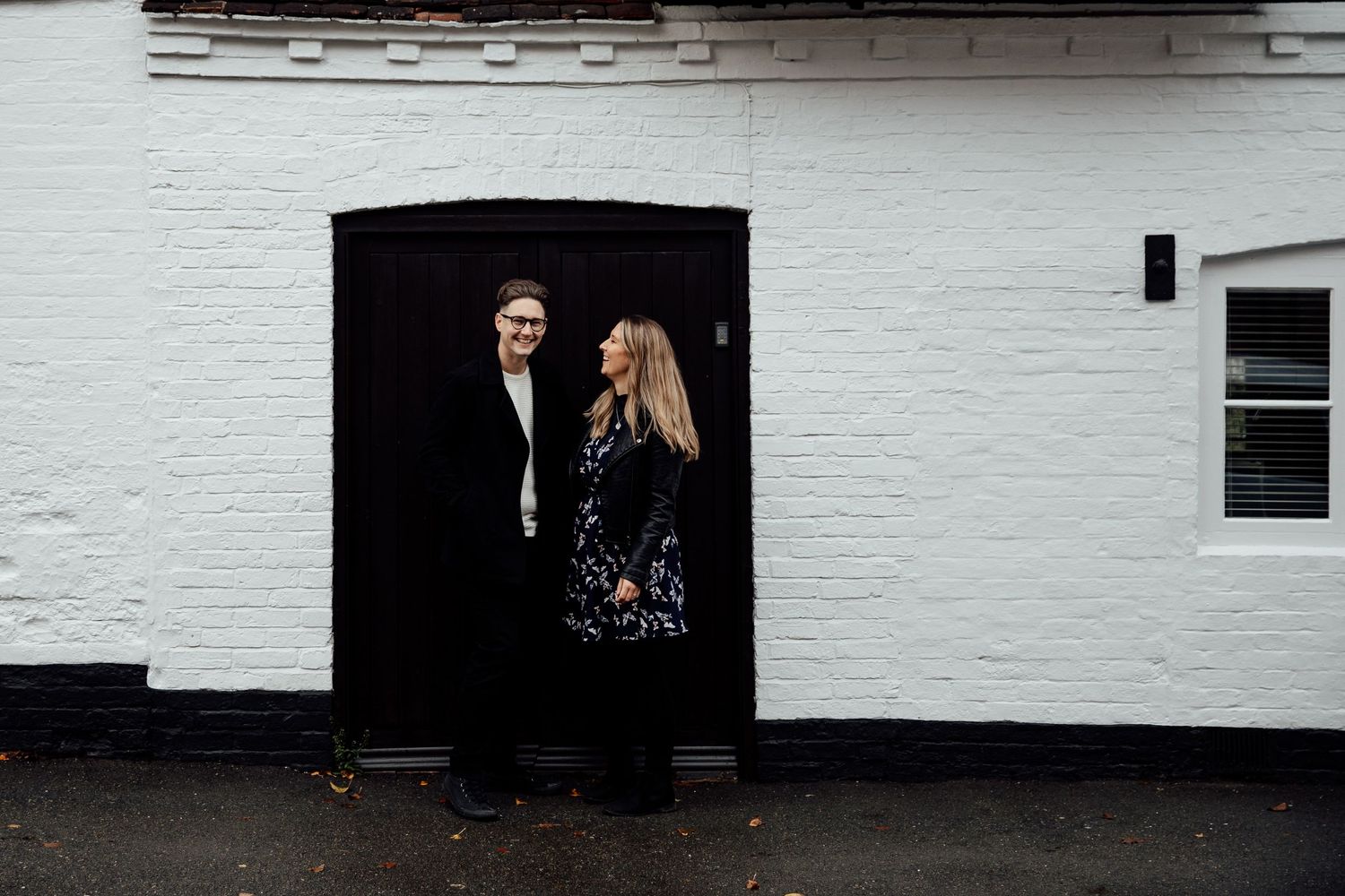 A couple poses against a white painted wall in a minimalist composition.