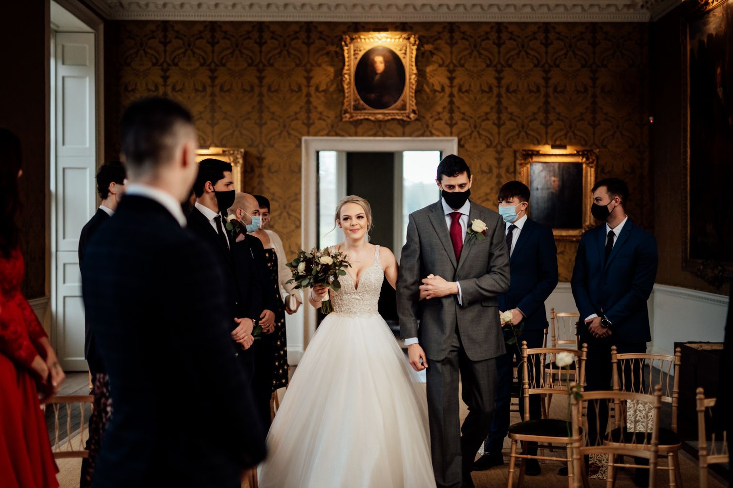 A wedding ceremony taking place in an elegant room with ornate wallpaper and vintage portraits.