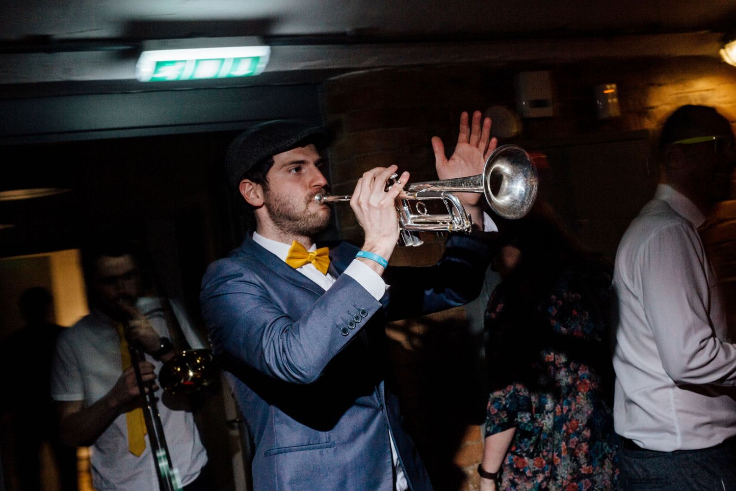 Musician in suit plays trumpet during evening wedding reception.