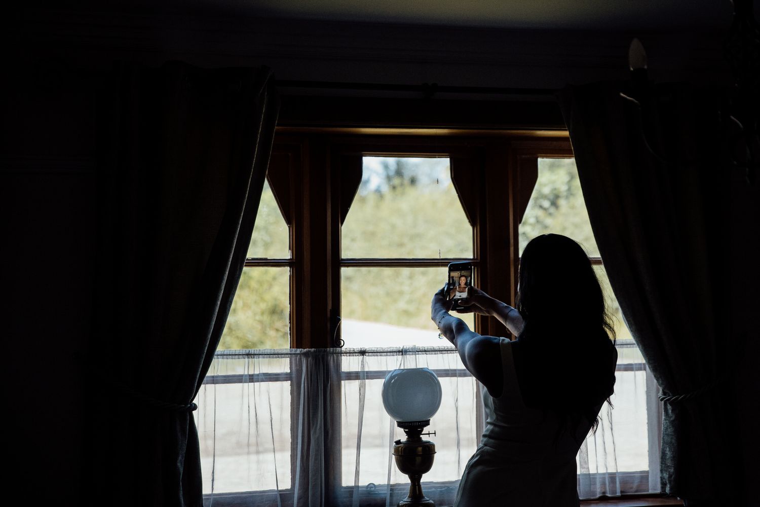 Silhouette of person getting ready by window with dramatic lighting and curtains.
