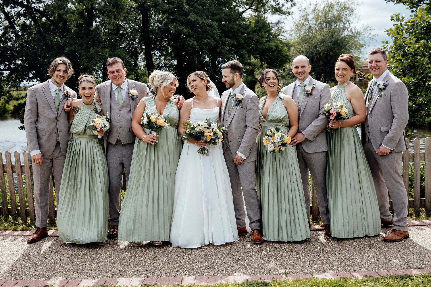 Wedding party group photo with bridesmaids in sage green dresses and groomsmen in grey suits.
